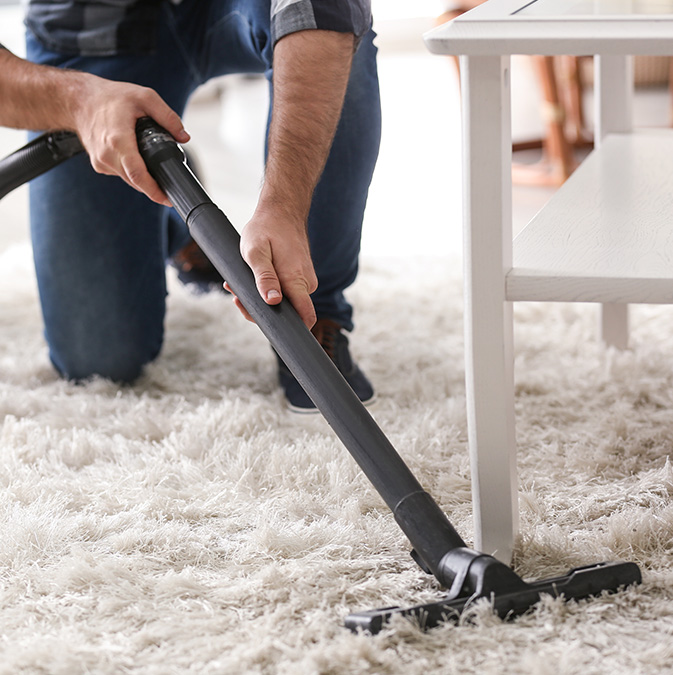 A man vacuuming a rug in a living room.