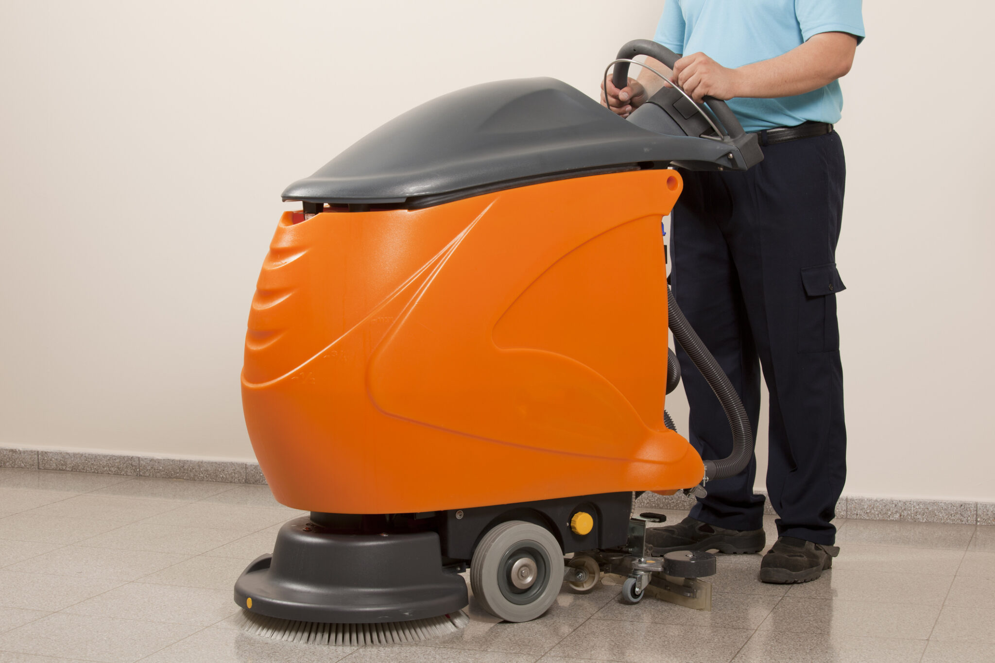 A man using a walk-behind floor scrubber in a room.