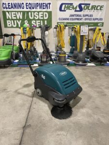A Tennant S6 25" Battery Powered Sweeper in a warehouse showroom.