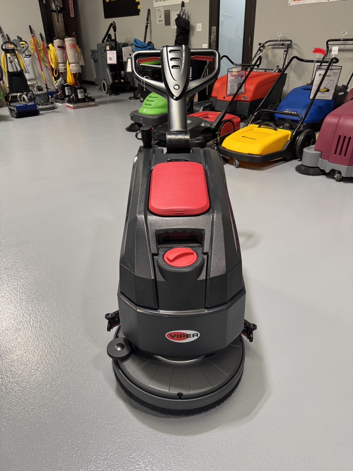 A Viper AS4325B 17" Walk-Behind Scrubber in a warehouse showroom at ChemSource Direct.