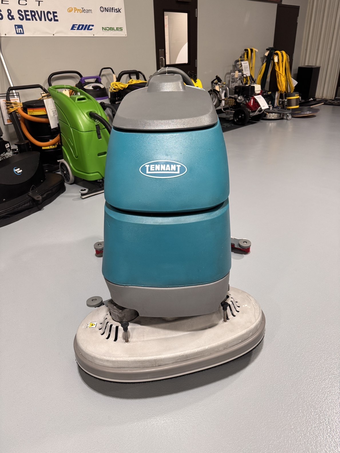 A Tennant T5 32" Walk-Behind Scrubber in a warehouse showroom at ChemSource Direct.