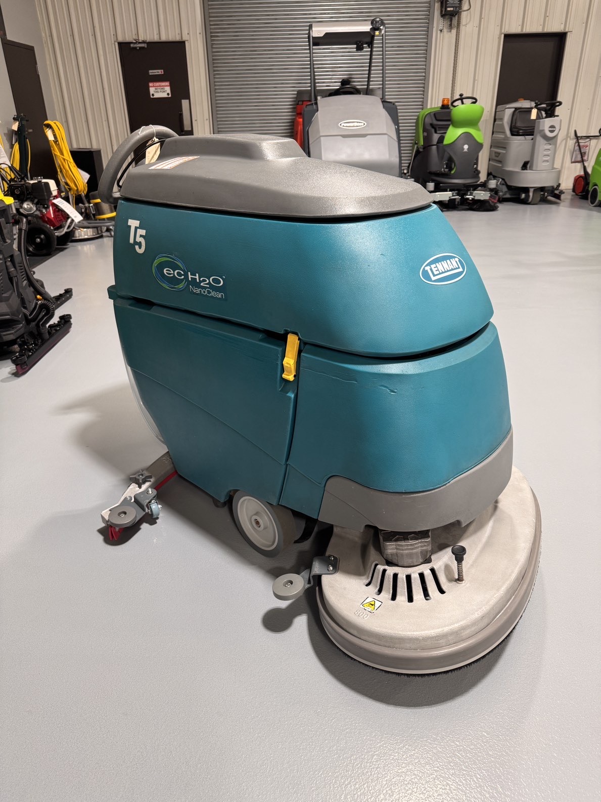 A Tennant T5 32" Walk-Behind Scrubber in a warehouse showroom at ChemSource Direct.