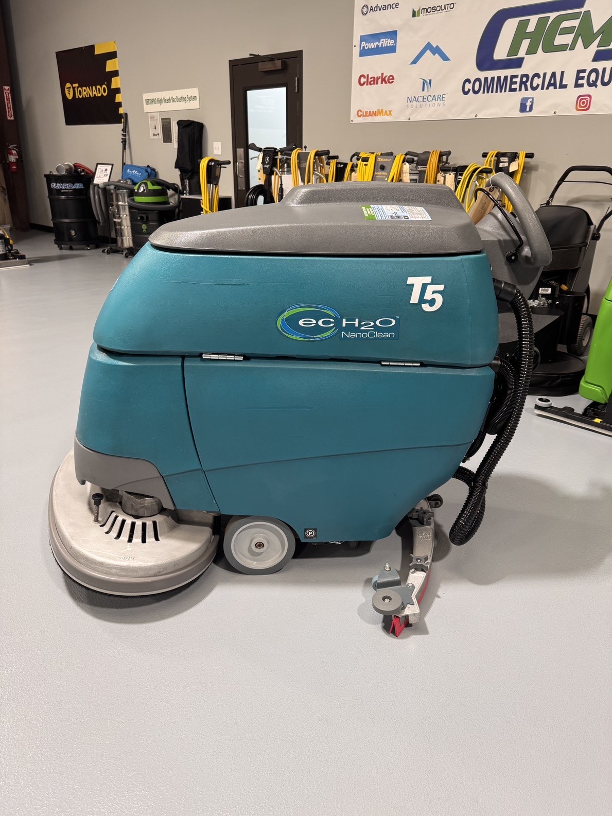 A Tennant T5 32" Walk-Behind Scrubber in a warehouse showroom at ChemSource Direct.