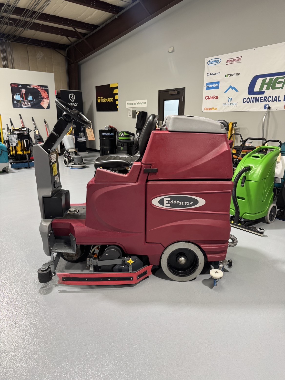 A Minuteman ERide 28/32 Cylindrical Ride-On Scrubber in a warehouse showroom at ChemSource Direct.