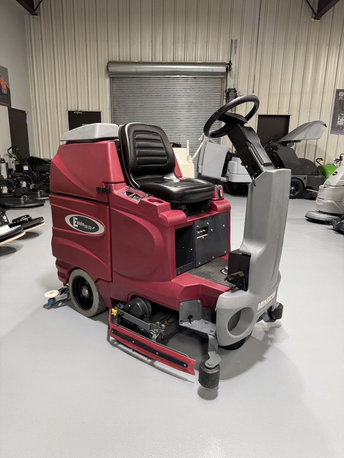 A Minuteman ERide 28/32 Cylindrical Ride-On Scrubber in a warehouse showroom at ChemSource Direct.