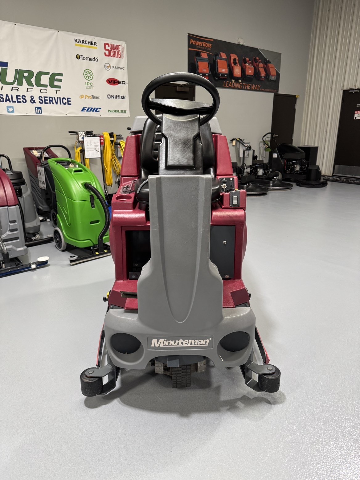 A Minuteman ERide 28/32 Cylindrical Ride-On Scrubber in a warehouse showroom at ChemSource Direct.