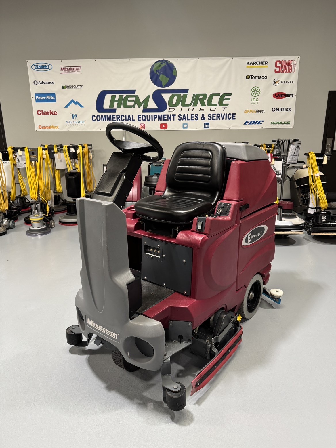 A Minuteman ERide 28/32 Cylindrical Ride-On Scrubber in a warehouse showroom at ChemSource Direct.